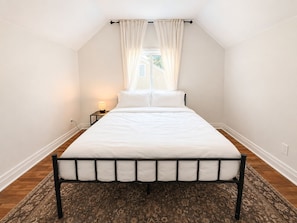 A bedroom with a bed, a nightstand, a lamp, a window with curtains, and a patterned rug. - Modern 4BR Home Near Downtown Winnipeg (Winnipeg)