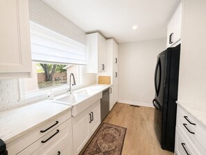A kitchen with white cabinetry, a black refrigerator, and a window with blinds. - Modern 4BR Home Near Downtown Winnipeg (Winnipeg)