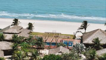A beachside resort with thatched-roof structures, a pool area, and palm trees.