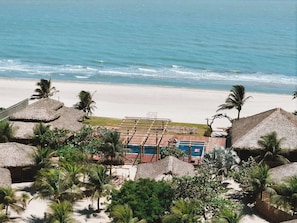 A beachside resort with thatched-roof structures, a pool area, and palm trees. - Canto dos Ventos Hotel (Cruz)