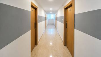 Un pasillo con puertas a ambos lados que conduce a una habitación luminosa con ventanas.