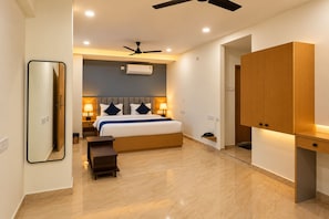 Une chambre d’hôtel comprenant un lit, des lampes de chevet, un ventilateur de plafond, un appareil de climatisation, une armoire en bois et un miroir.