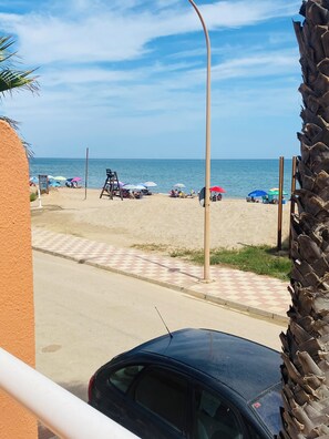 Ein Strand mit Sonnenschirmen, einem Rettungsschwimmerstand und einem am Rande geparkten Auto.
