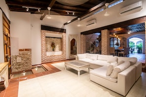 A spacious living area with a white sofa, a coffee table, and a stone fireplace. There is a brick wall and a wooden ceiling. - Luxury 5 Bdrm Villa Walled City (Cartagena de Indias)