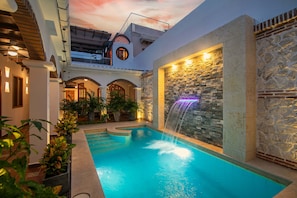 An indoor swimming pool with a waterfall feature, surrounded by stone walls and potted plants. - Luxury 5 Bdrm Villa Walled City (Cartagena de Indias)