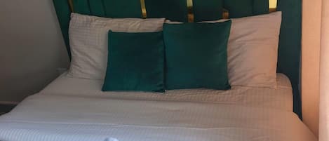 A bed with a green headboard, white bedding, and a white towel.