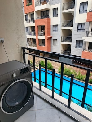 Ein Balkon mit Waschmaschine, Pool und einem mehrstöckigen Gebäude im Hintergrund.