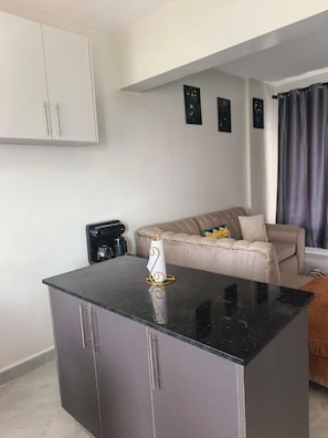 Eine moderne Küche mit schwarzem Arbeitsplatz, einer Kaffeemaschine und einem beigen Sofa im Wohnbereich.