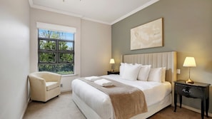 Habitación de hotel con una cama grande, dos lámparas de noche, una silla y una ventana con vista a árboles.