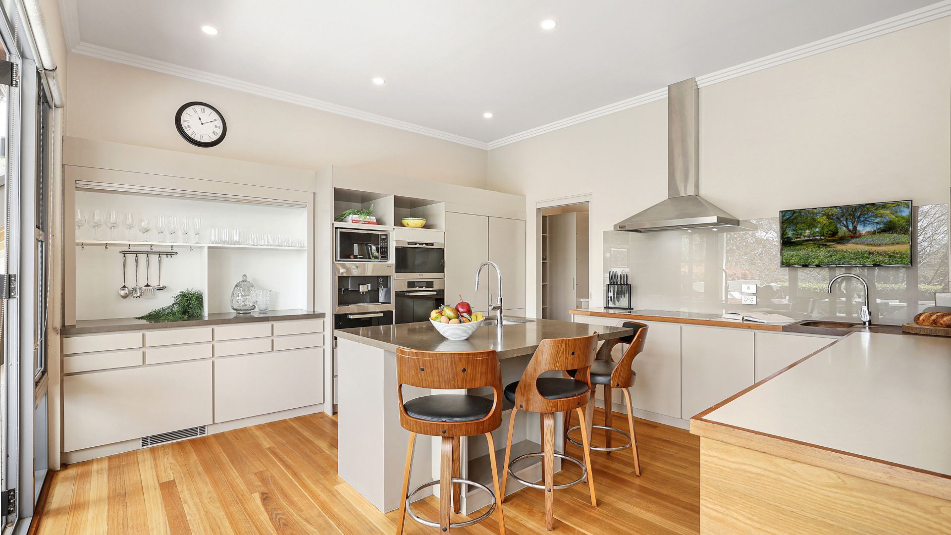 A modern kitchen with a central island, bar stools, a built-in oven, and a large window.