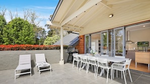 Een terras buiten met een eettafel en stoelen, een barbecue en een zithoek met lounge fauteuils.