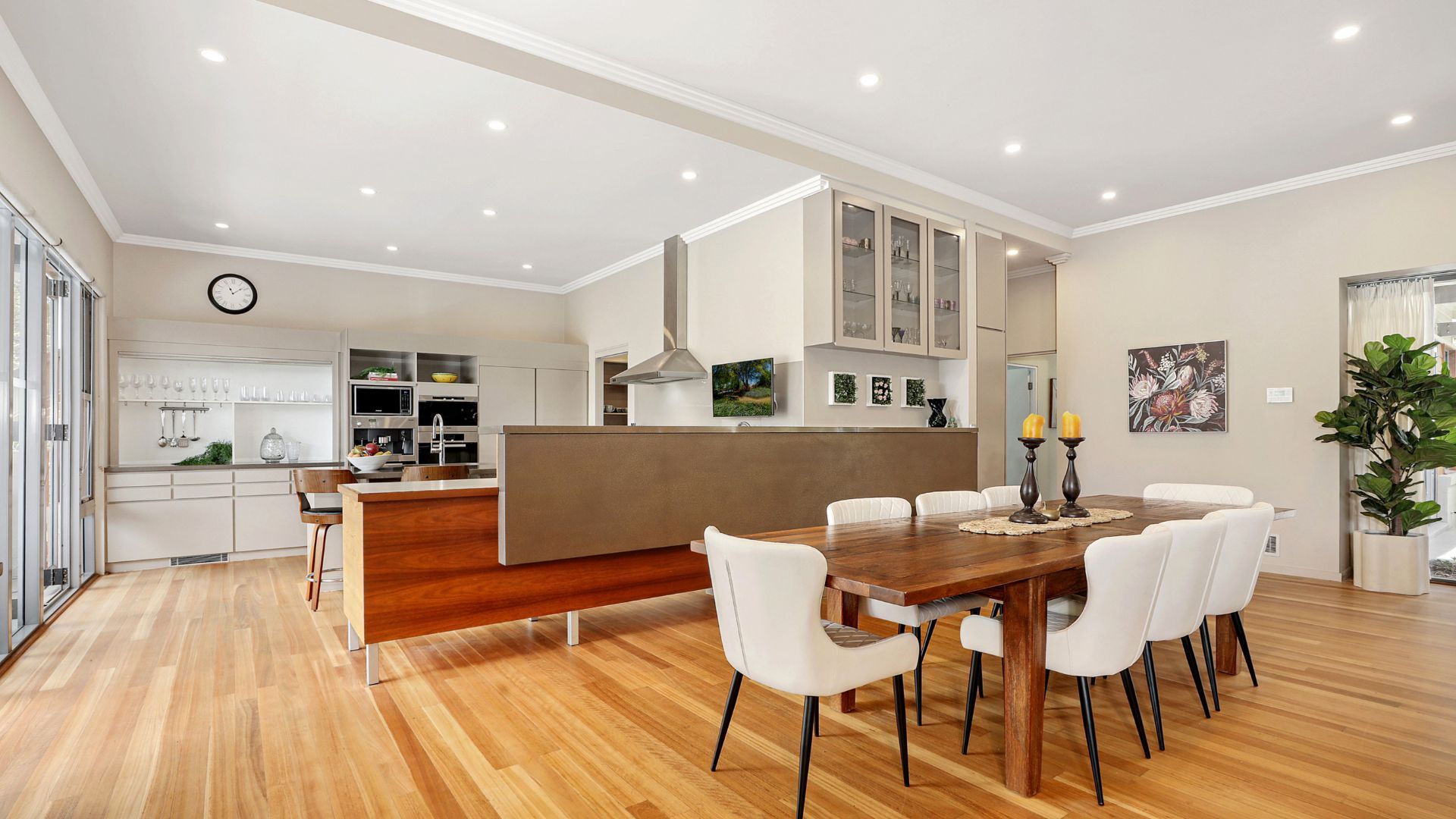 A modern kitchen with a central island, white cabinetry, and a dining area with a wooden table and white chairs.