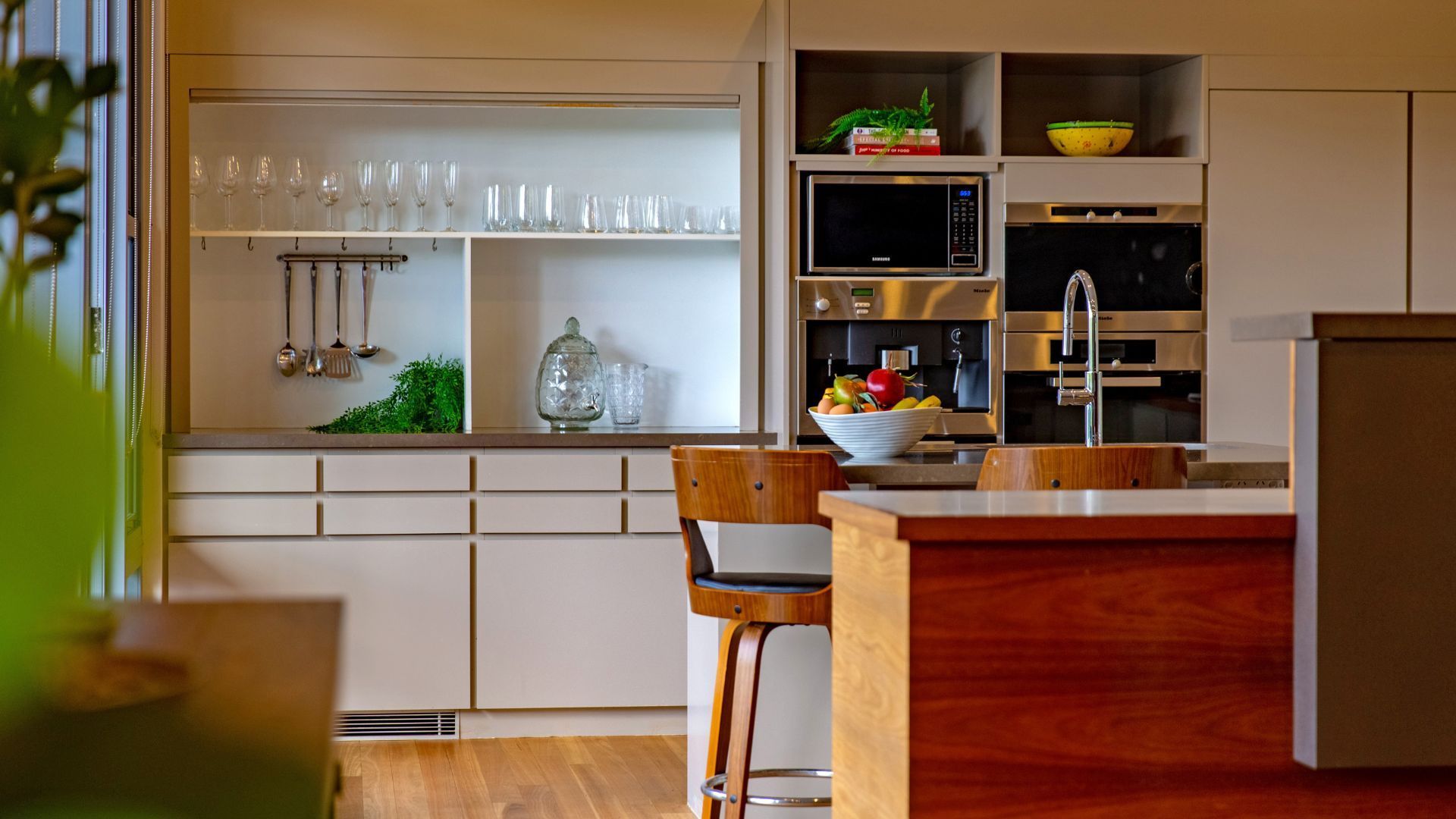 Una cocina moderna con una isla central, electrodomésticos integrados y una estantería con puertas de cristal.