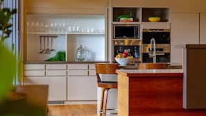 Una cocina moderna con una isla central, electrodomésticos integrados y una estantería con puertas de cristal.