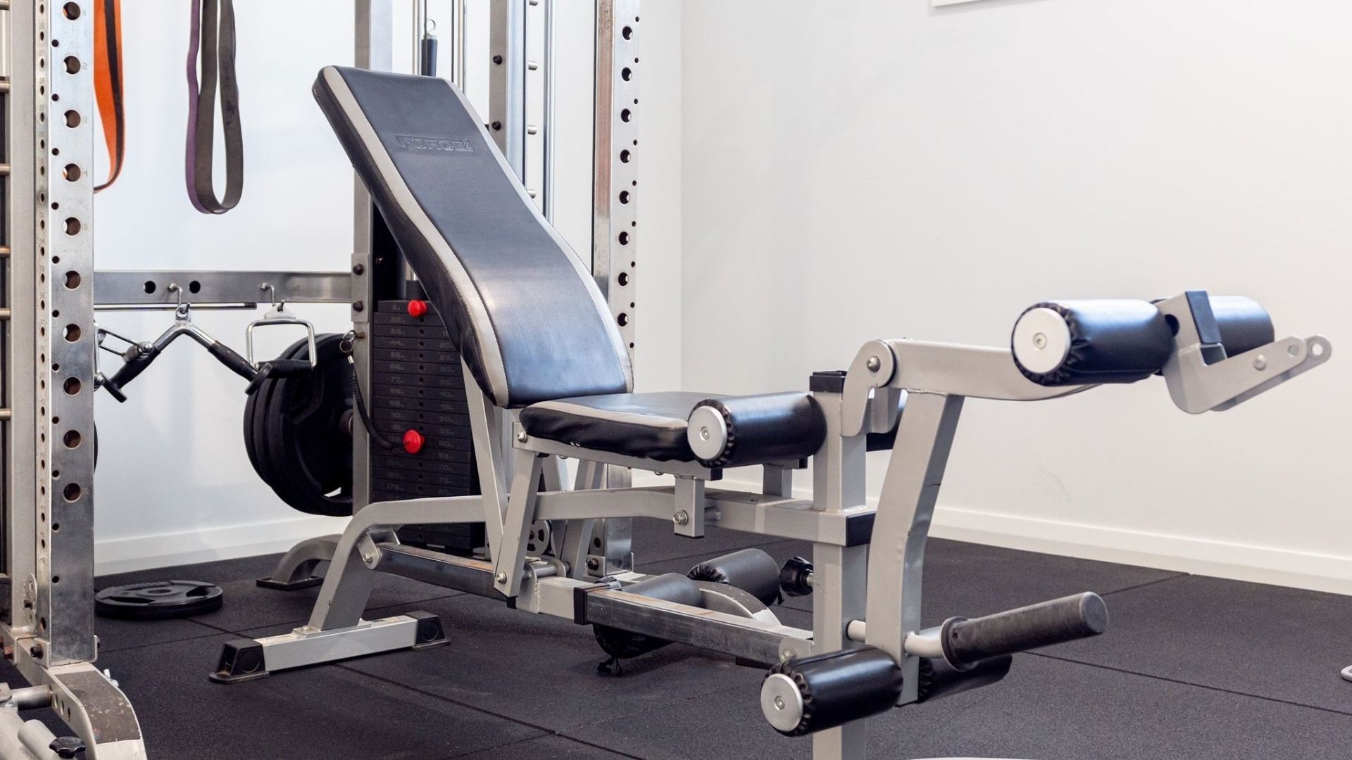 Een sportschool met een bankdrukapparaat, gewichtstapel en diverse fitnessapparaten.