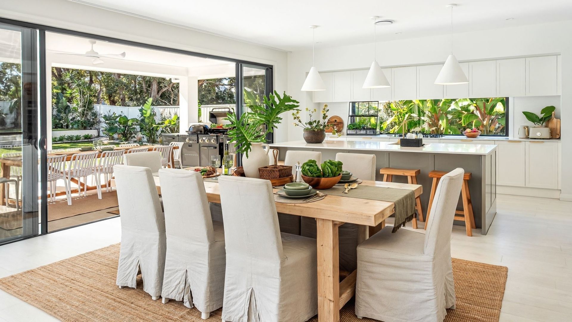 A modern kitchen with white cabinets, a dining area with a large table and chairs, and a view of the outdoors.