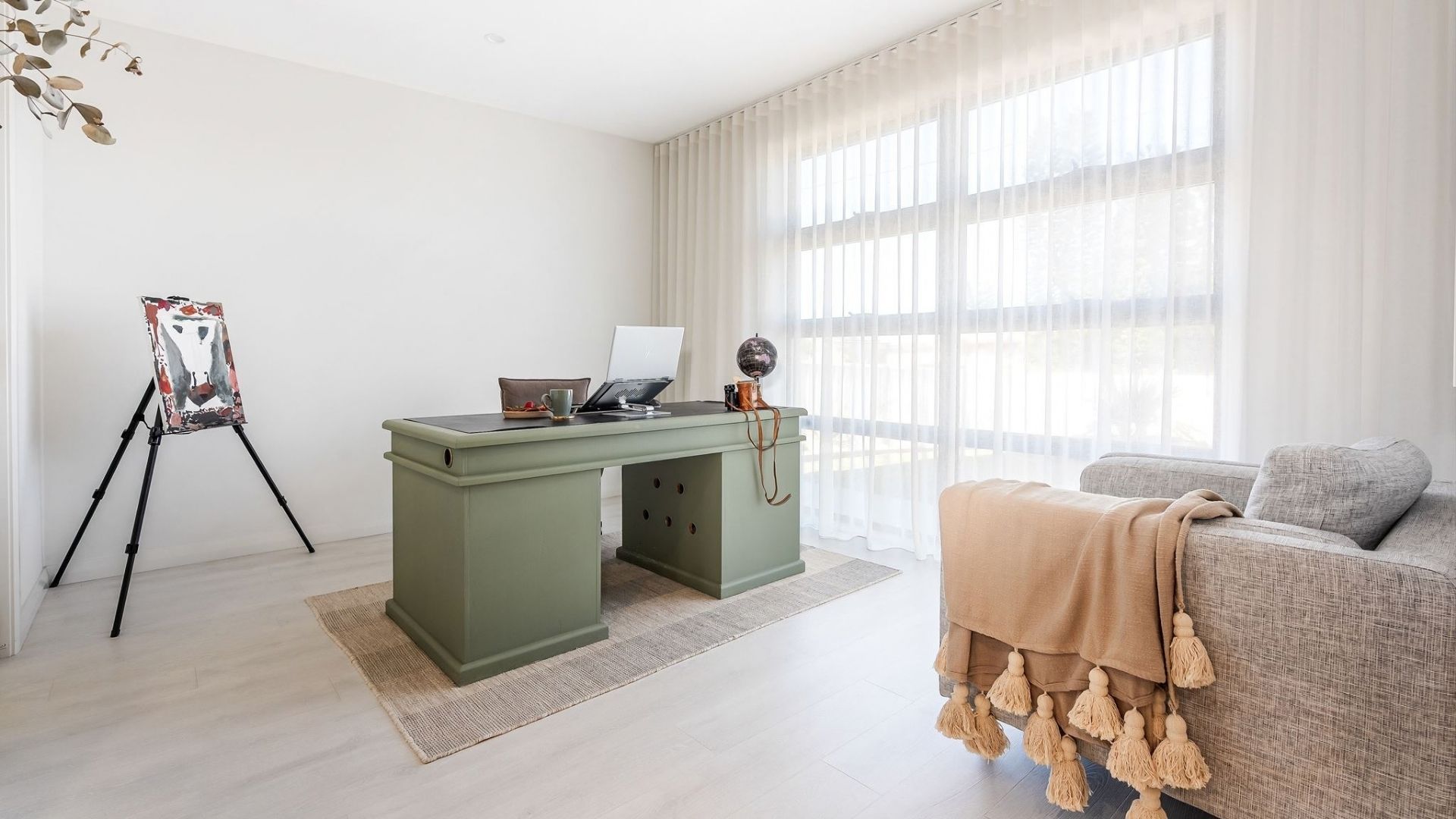 A minimalist room with a desk, a bed, and a window with sheer curtains.