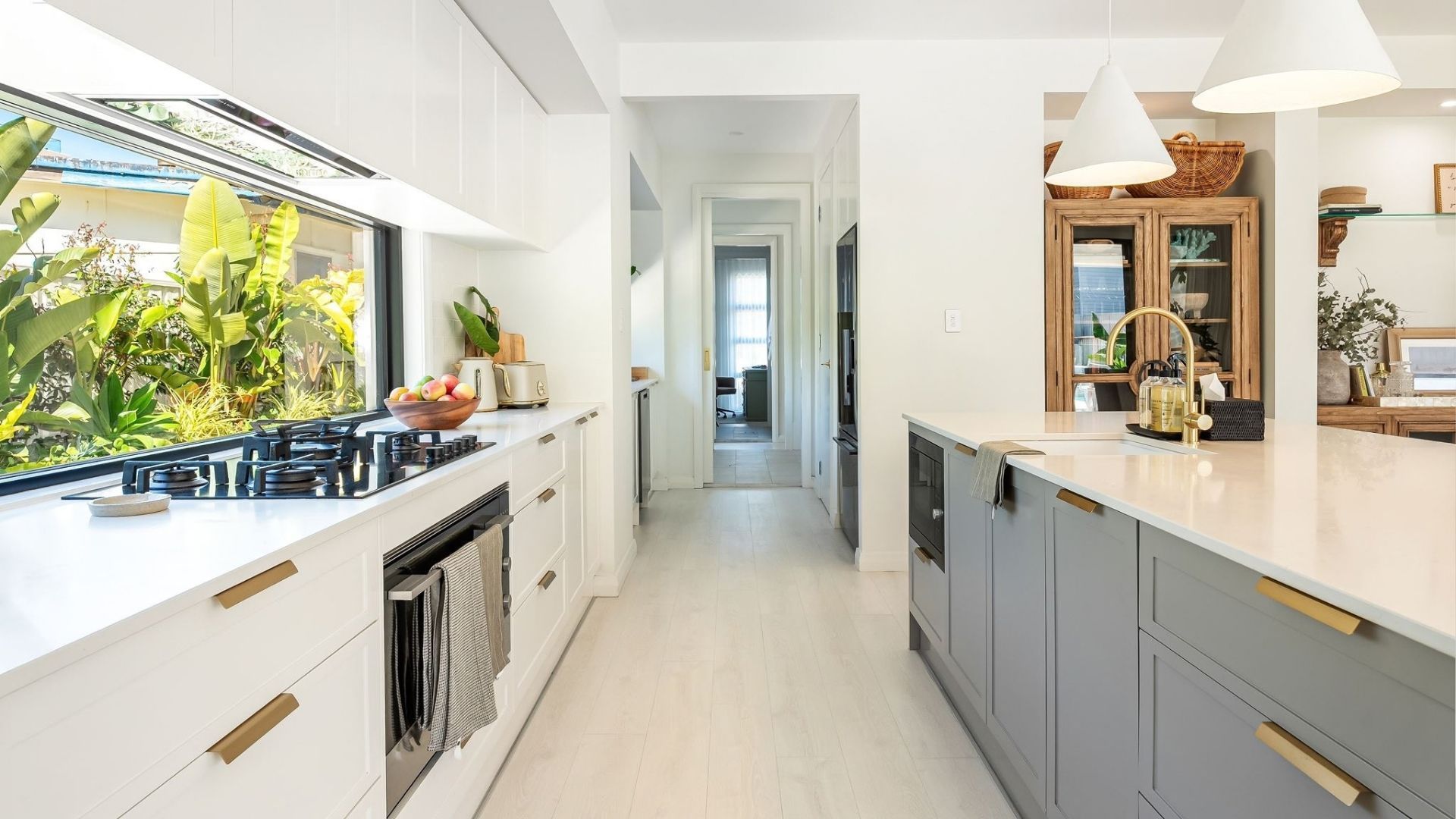 Een moderne keuken met een centraal eiland, een fornuis en uitzicht op een balkon met planten.