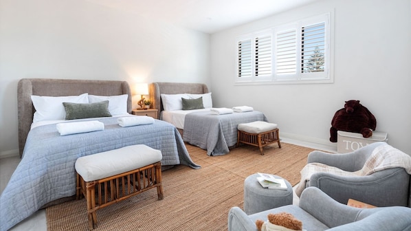 A hotel room with two beds, a sitting area with a chair and ottoman, a window with shutters, and a teddy bear on a shelf. - Palma – amazing coastal oasis at Callala Beach in beautiful Jervis Bay (Callala Beach)
