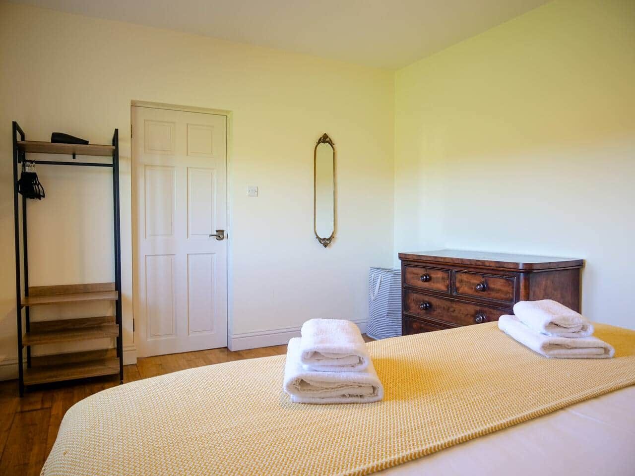 A bedroom with a bed, a dresser, a mirror, and a shelf unit.