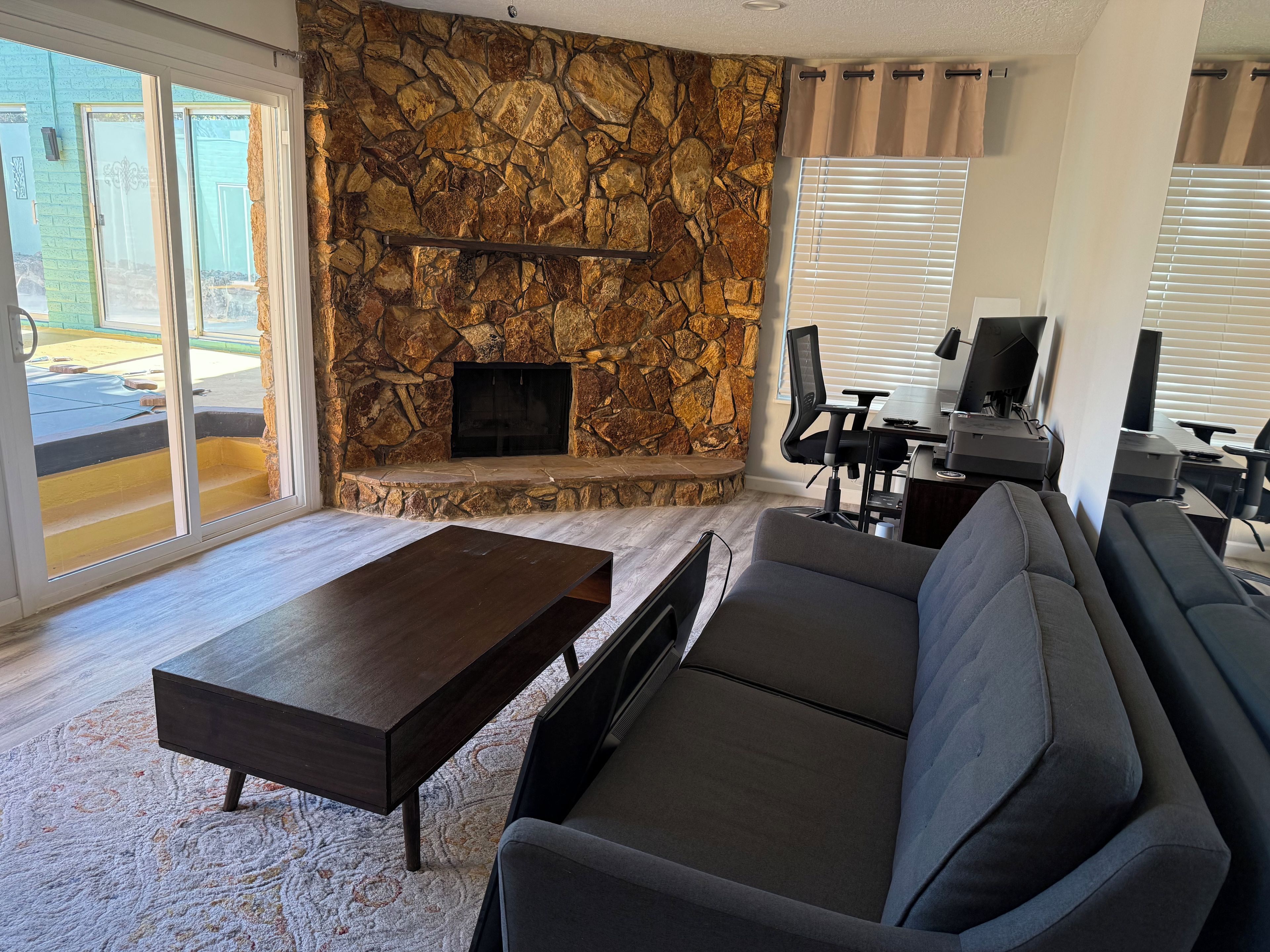 A living room with a stone fireplace, a sofa, a coffee table, and a computer desk.