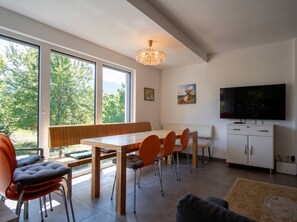 Ein modernes Interieur mit Essbereich, Sitzgelegenheiten, einem Fernseher und Blick auf Grünflächen.