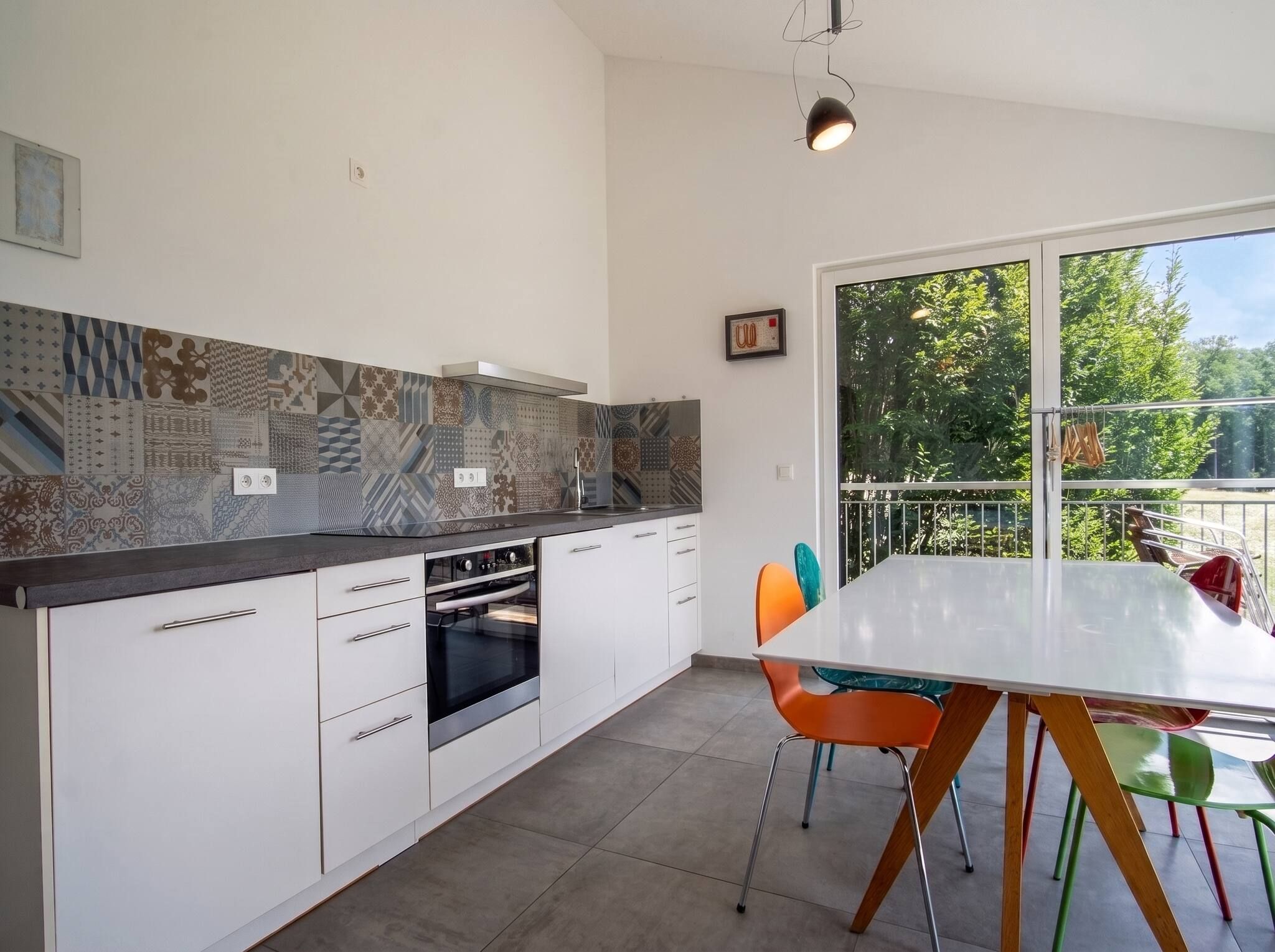 Eine moderne Küche mit weißen Schränken, einem eingebauten Ofen und einem großen Fenster mit Blick auf Grünflächen.