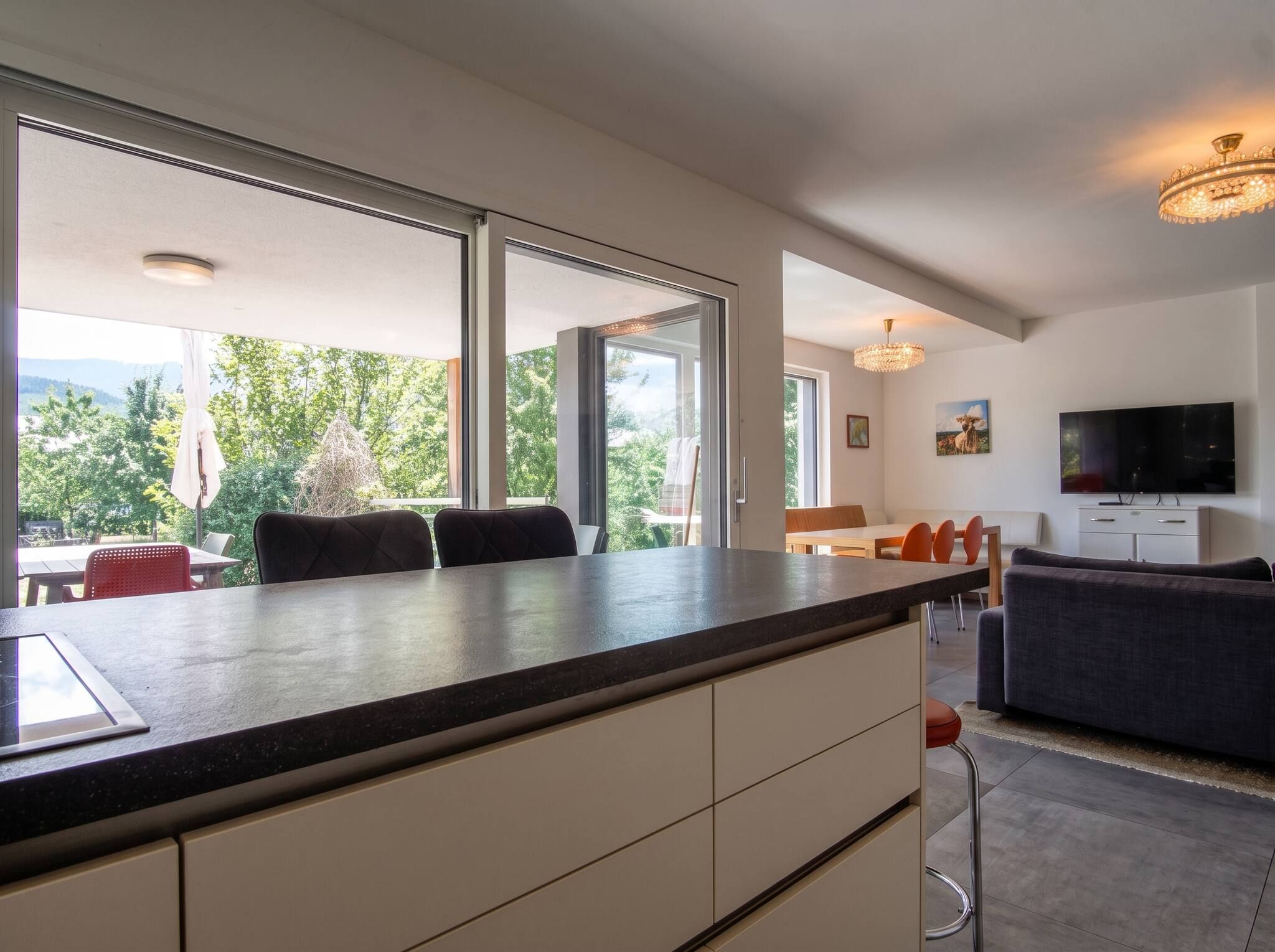Eine moderne Küche mit einer großen Kochinsel, ein Essbereich mit Stühlen und ein Wohnzimmer mit Sofa und Fernseher.