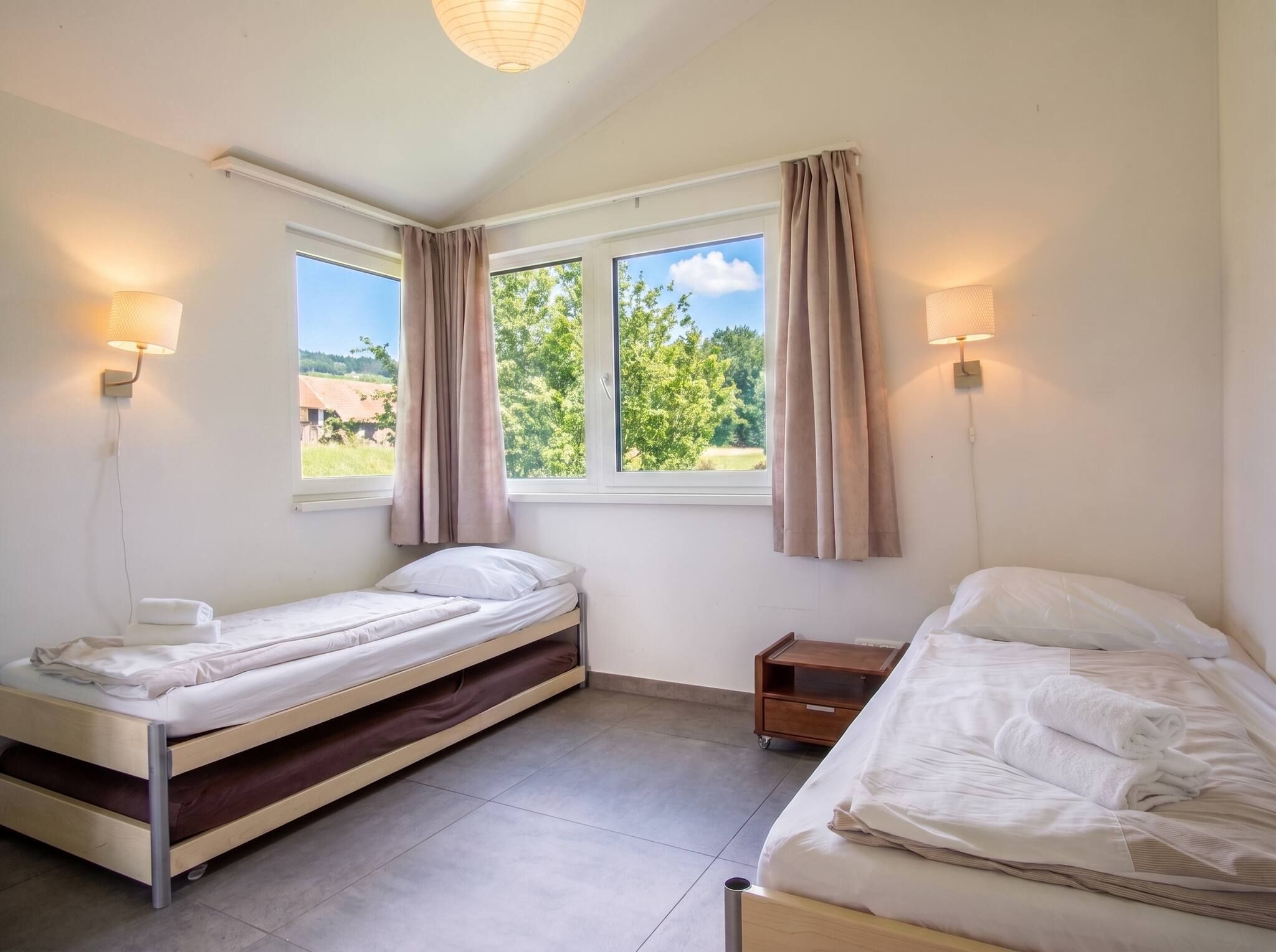 A bedroom with two beds, a window with curtains, and wall-mounted lamps.