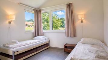 A bedroom with two beds, a window with curtains, and wall-mounted lamps.