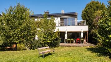 A modern two-story house with a balcony, a grassy yard, and a bench.