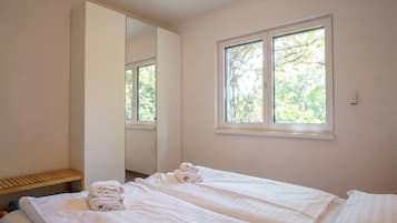 A hotel room with a bed, a mirror, a window, and a wooden shelf.
