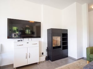 A modern living room with a flat-screen TV mounted on a white cabinet, a black entertainment unit with shelves, and a green armchair. - Lichtblick Garden - Near the Lake by WÖRTHWHILE (Seeboden)