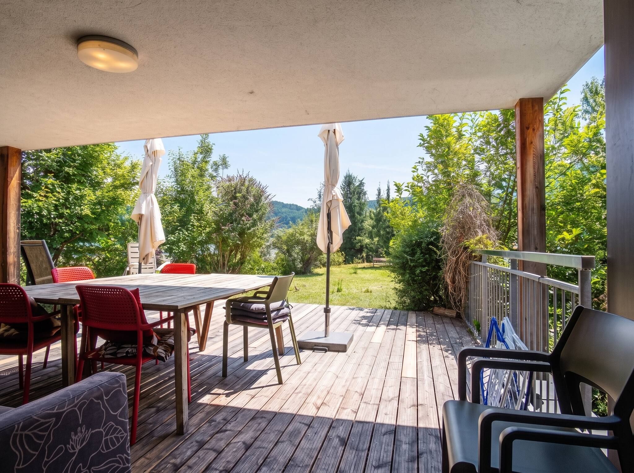 An outdoor deck with a table and chairs, surrounded by greenery and trees.