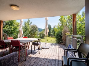 An outdoor deck with a table and chairs, surrounded by greenery and trees. - Lichtblick Garden - By the Lake by WÖRTHWHILE (Seeboden)
