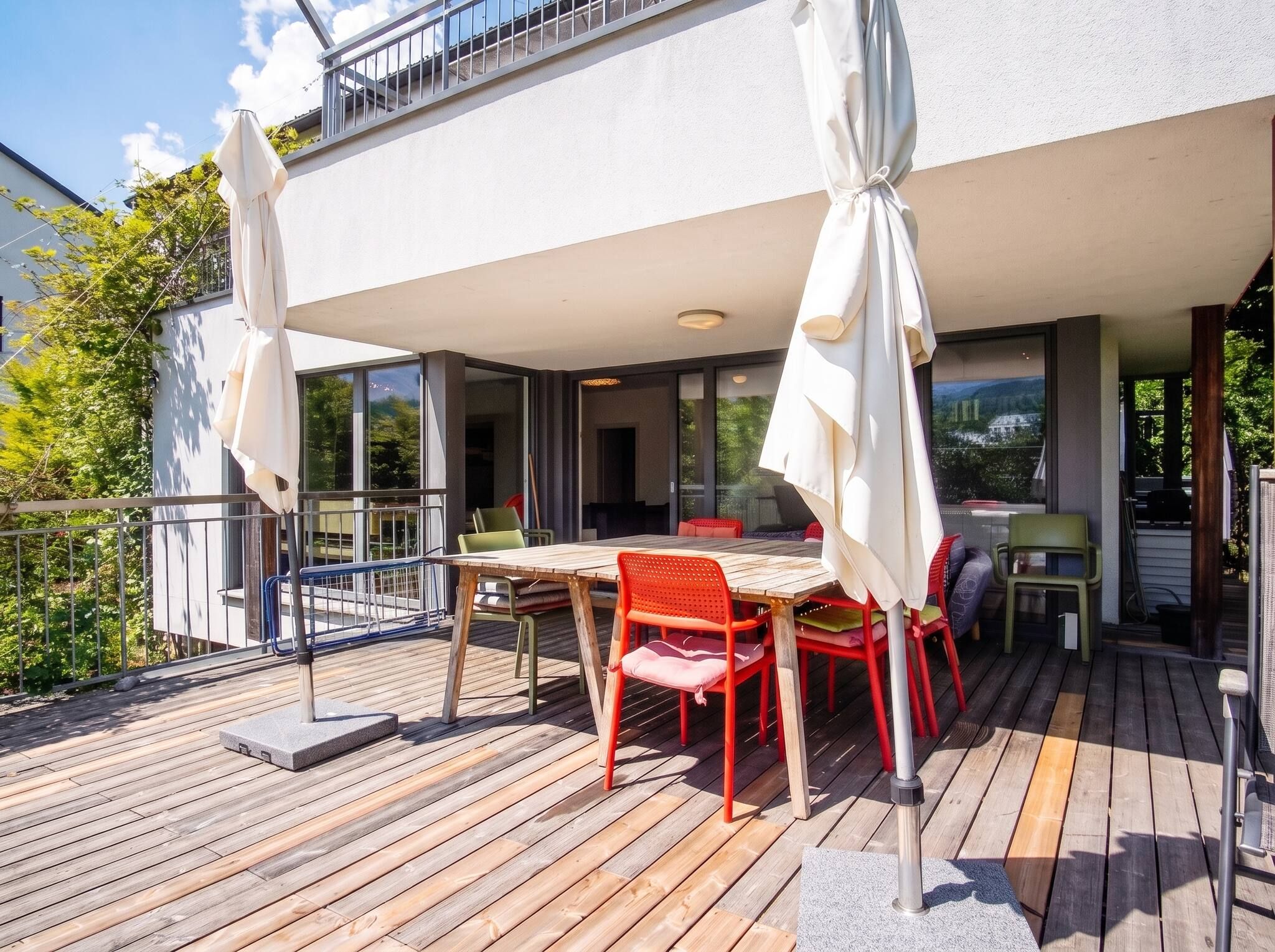 A wooden deck with a table and chairs, a covered seating area, and a balcony with a railing.