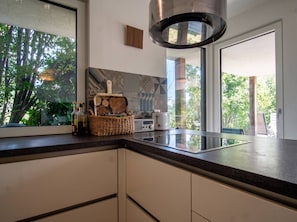 A modern kitchen with a large window, a built-in stove, and a hanging light fixture. - Lichtblick Garden - Near the Lake by WÖRTHWHILE (Seeboden)
