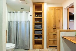 Un baño con cortina de ducha, inodoro, repisa de madera con toallas dobladas y armarios de madera.