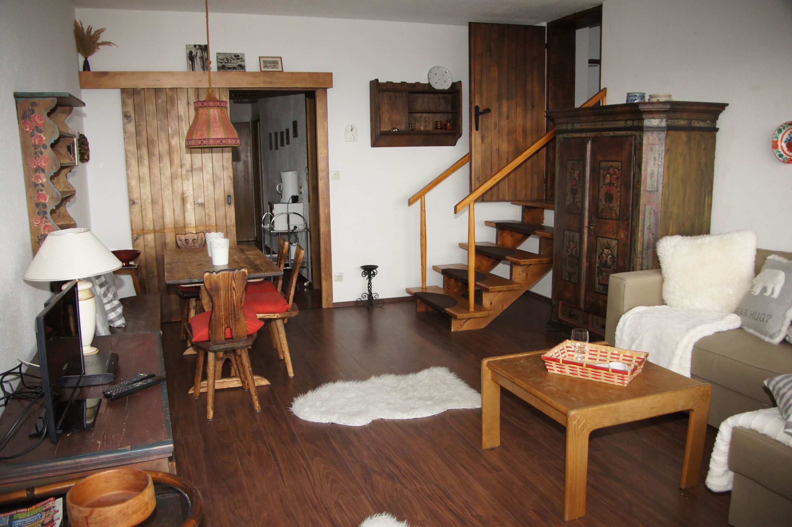 A cozy living room with a wooden dining table, a sofa, a white furry rug, and a staircase.