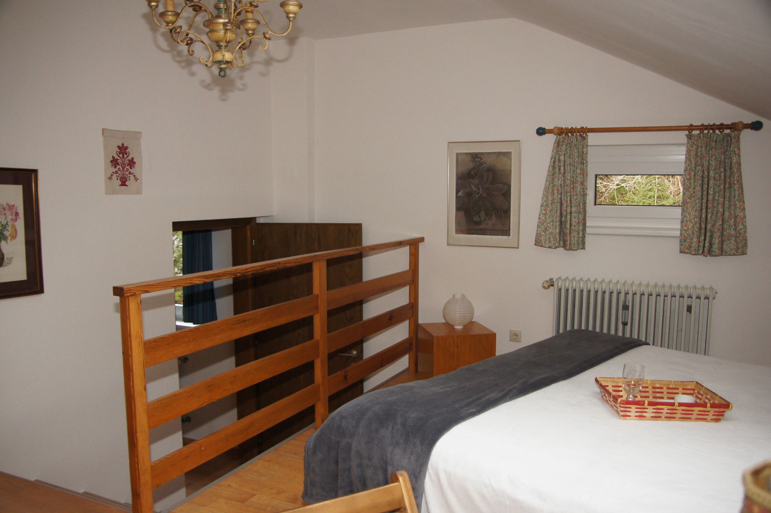 Un dormitorio con una cama litera de madera, una mesita de noche, un radiador y una ventana con cortinas.