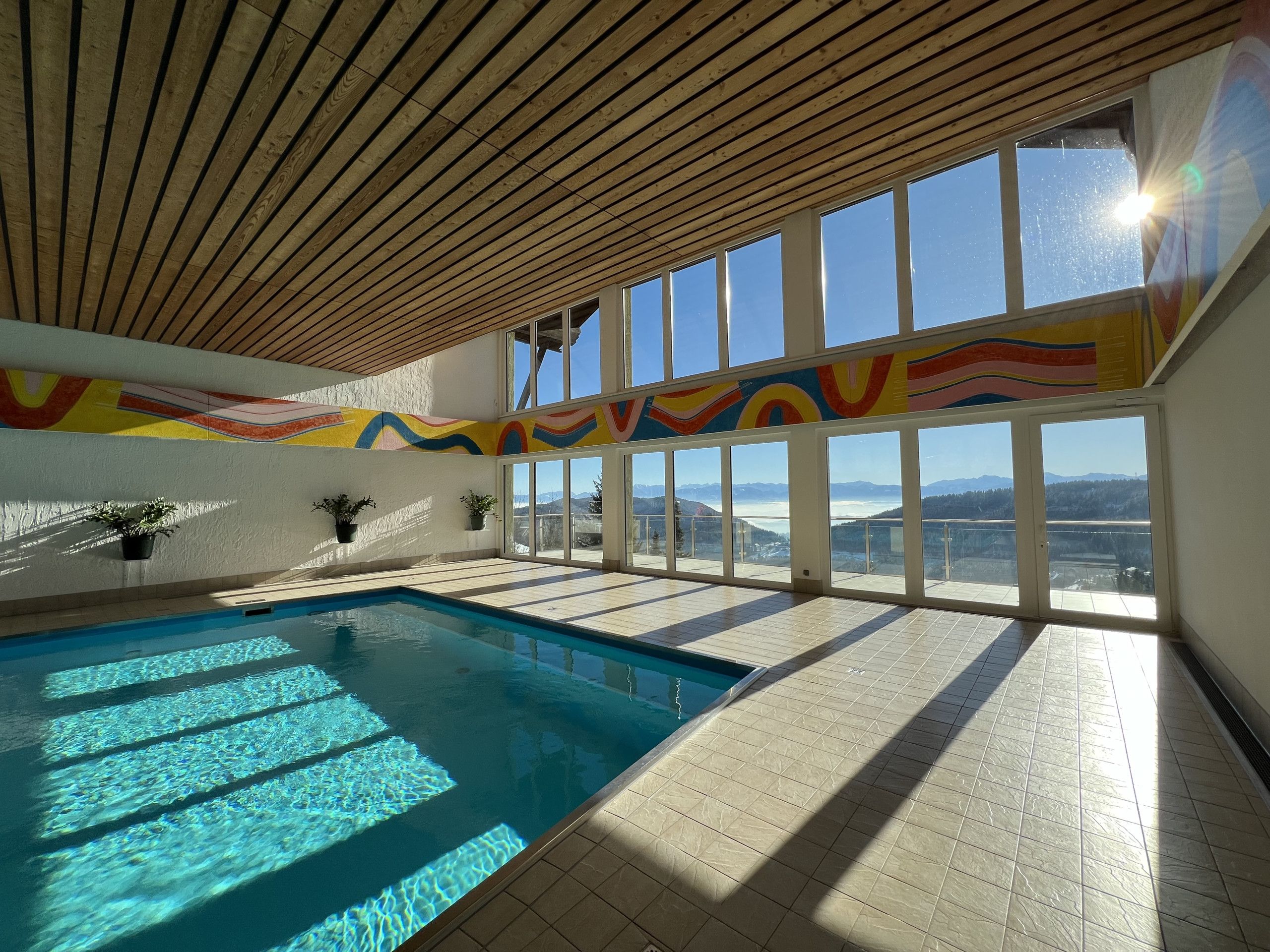Piscina interior con vistas a montañas a través de grandes ventanales.