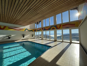 Piscina interior con vistas a montañas a través de grandes ventanales.