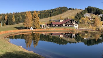A lakeside property with a wooden building, a fenced area, and a reflection in the water.