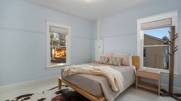 A bedroom with a bed, a nightstand, a window, and a coat rack.