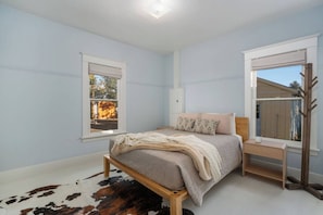 Een slaapkamer met een bed, nachtkastje, raam en kapstok.