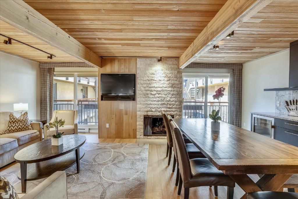 A modern living room with a fireplace, wooden ceiling, and a large dining table.