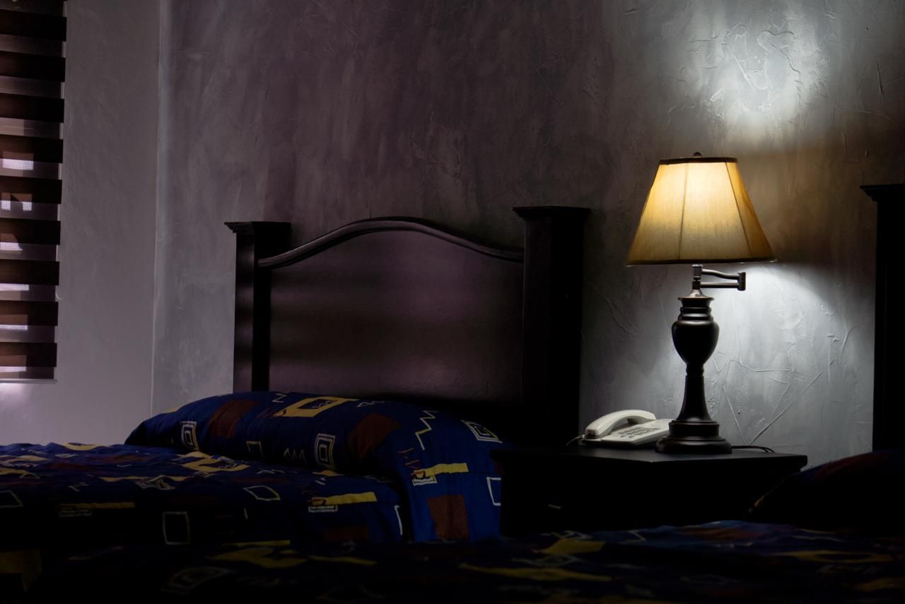 A bedroom with a bed, a nightstand with a lamp, and a wall with a textured pattern.