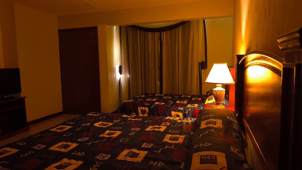 Una habitación de hotel con cama, lámpara, cortinas y televisión.