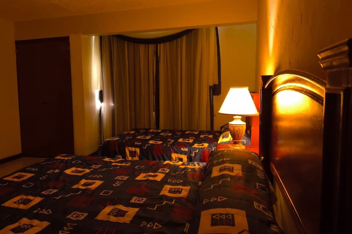 Ett hotellrum med en säng, en lampa, gardiner och en tv.