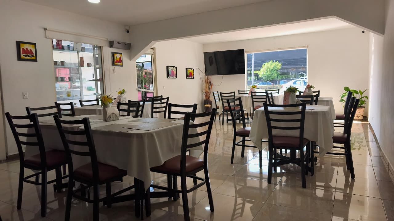 A dining area with multiple tables and chairs, a television mounted on the wall, and a view of the outdoors through a window.